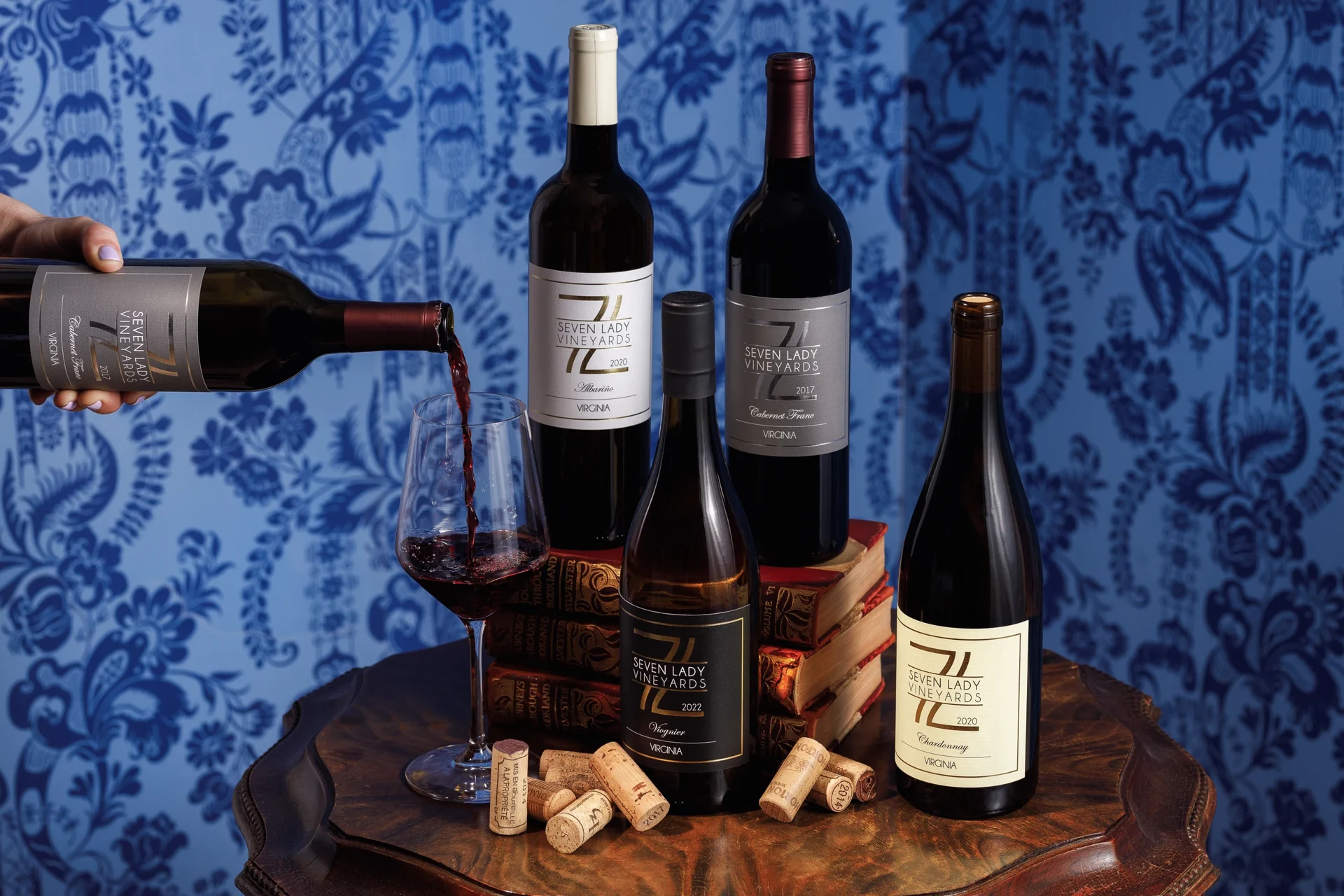 7 Lady Vineyards wines on a wooden table, with a glass of Cabernet Franc being poured